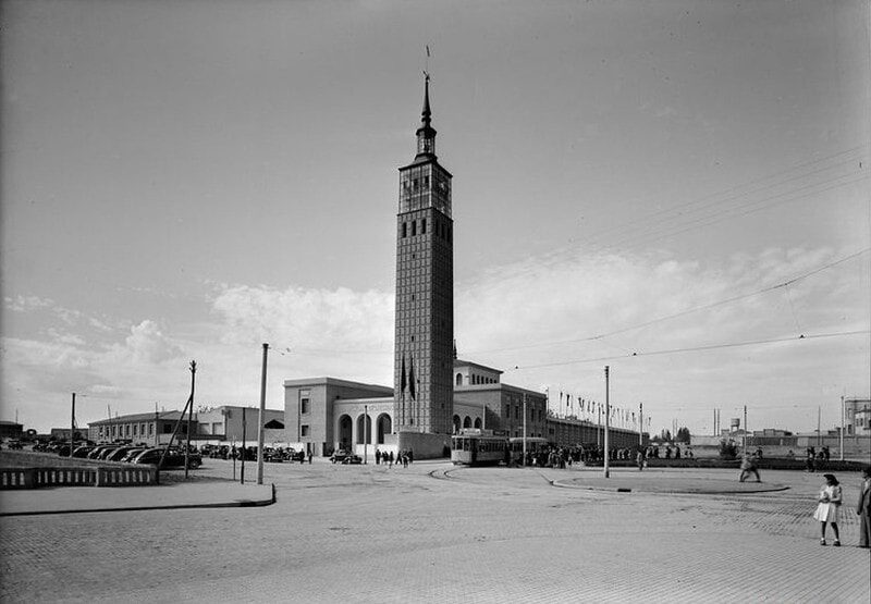 Fotografía en blanco y negro del recinto de la Feria de Muestras de Zaragoza con su torre, tranvía y coches de época