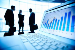 Financial document in laptop on background of three business partners having meeting